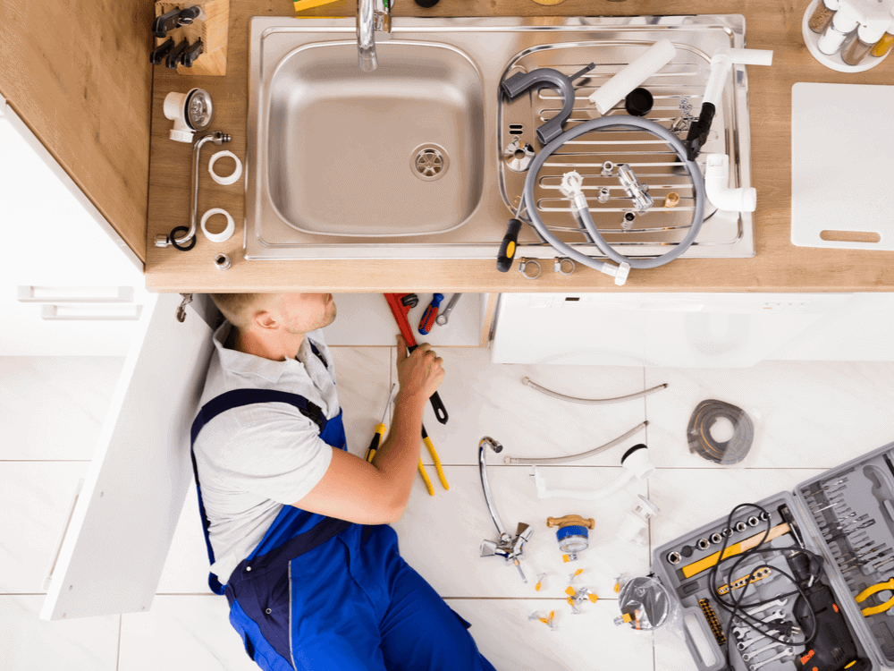 Plumber repairing a kitchen sink with tools laid out